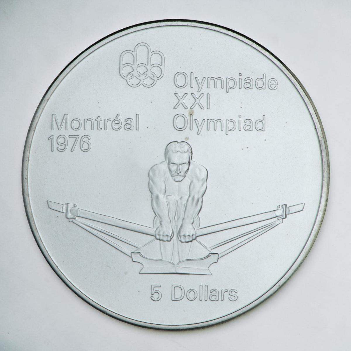 Coin, silver, competitive rower facing viewer, pressing oars up and away.