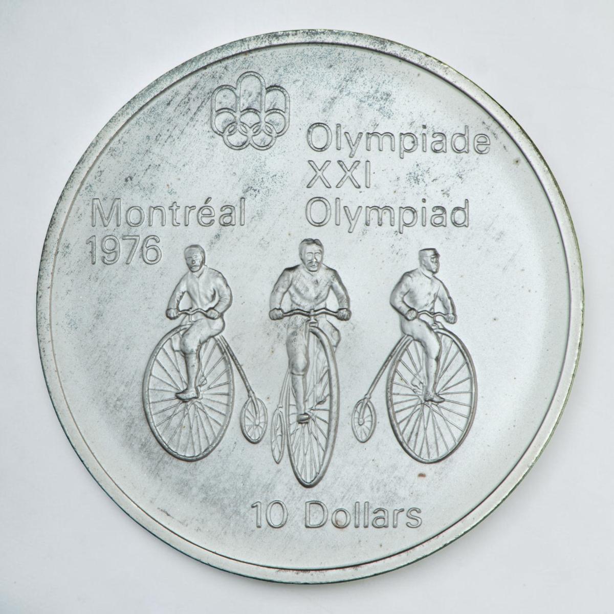 Coin, silver, 3 men riding tall-wheeled bicycles toward viewer.