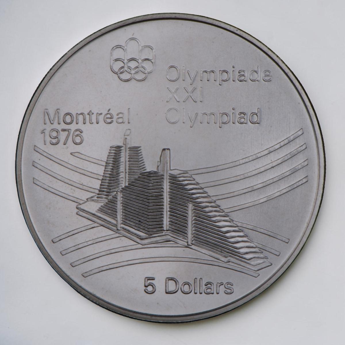 Coin, silver, 2 tall, narrow, triangular buildings, curved line motif behind.