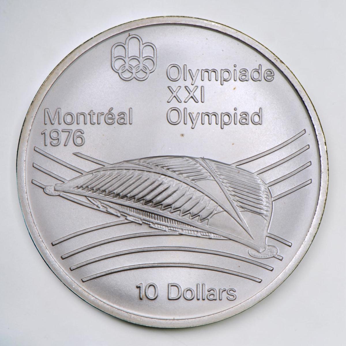 Coin, silver, low, oval building with domed, slotted roof, curved line motif behind.