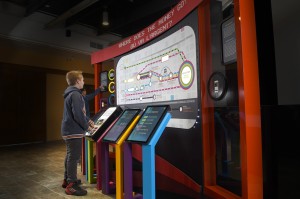 boy standing at a set of touch screens and a large route map