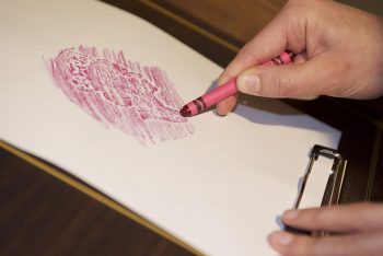 hands making a crayon rubbing of a coin