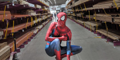 Man in a superhero costume crouching in an aisle of a home renovation warehouse.