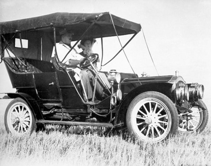 A black and white photo of a car from before the First World War in a field.