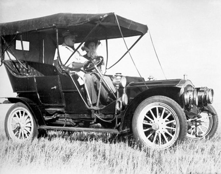 A black and white photo of a car from before the First World War in a field.