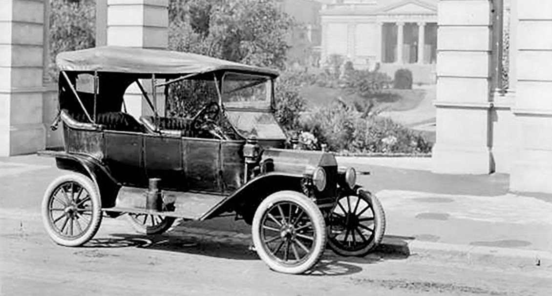 A historic photo of a car from before the First World War parked in front of public buildings.