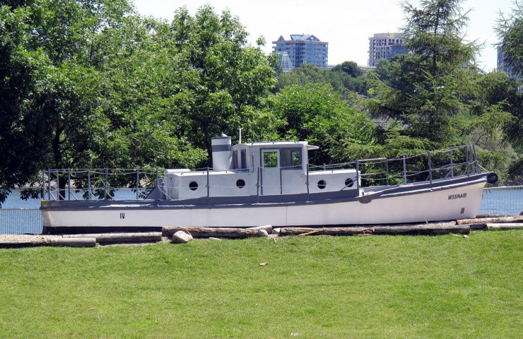 Photo, colour, small white boat with a cabin and smokestack, sitting on land in a park setting.