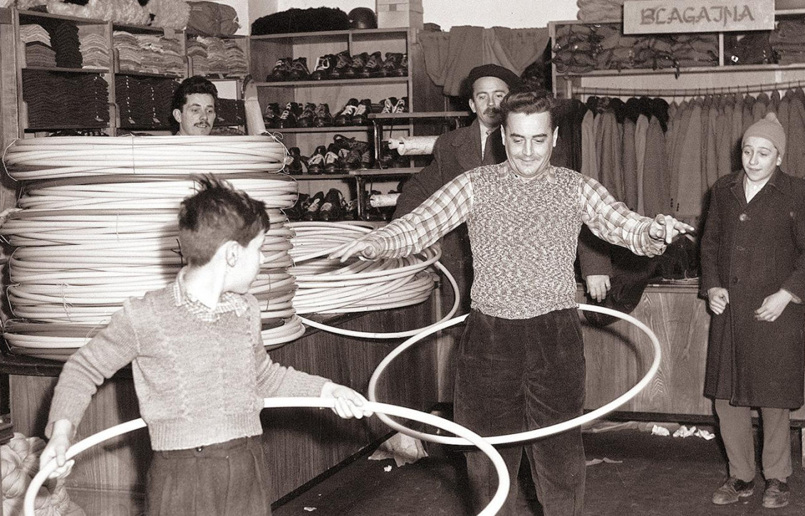 Photo, black and white, a man and a boy in a clothing store, swinging big hoops around their hips.