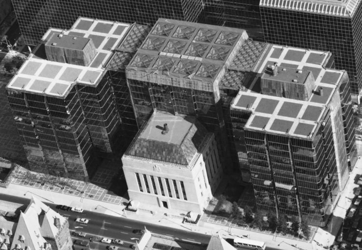 Photo, 3 attached glass buildings surrounding a square, stone building.