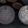 In front of a set of coins in a case, two coins, one lead, one silver, each with identical wreaths of maple leaves.
