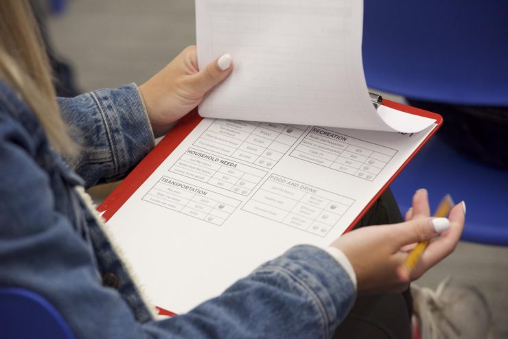 A teenager holding a clipboard in her lap filling in a form.