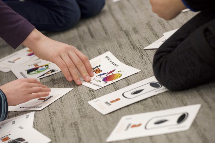 Children’s hands laying down brightly coloured game cards with cartoon images on them.