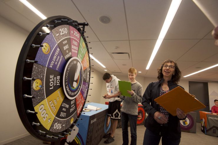 Two people with clipboards turning a colourful, roulette-style wheel.