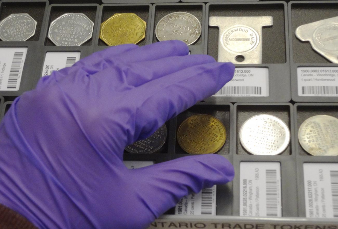 Hand in a purple glove reaching to touch a coin.