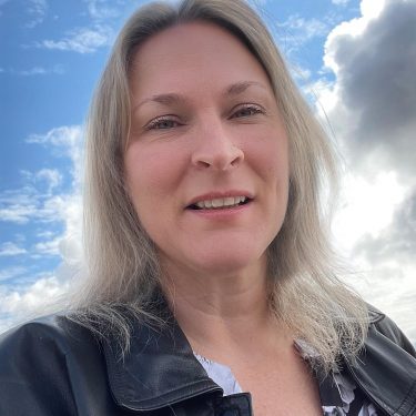 Photograph, woman, long hair, smiling, cloud filled sky behind her head.