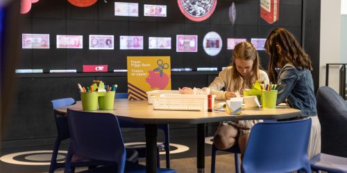 Photo, two young girls drawing at a table in a museum environment.