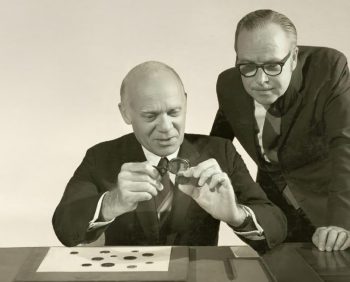 Governor Louis Rasminsky and Curator Sheldon S. Carroll Black-and-white photo of two men in suits examining coins.