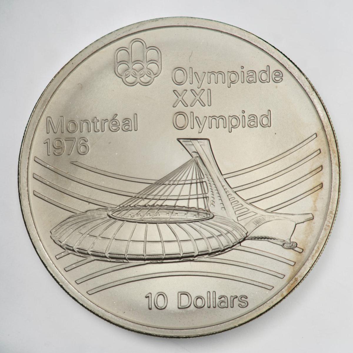 Coin, silver, low, oval stadium with tower at one end, curved line motif behind.
