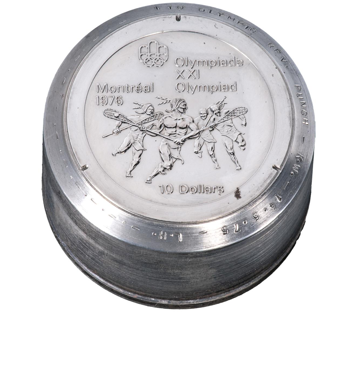 Grey metal cylinder with an engraving of Indigenous men playing lacrosse, with a logo of linked rings and the text Montréal 1976.