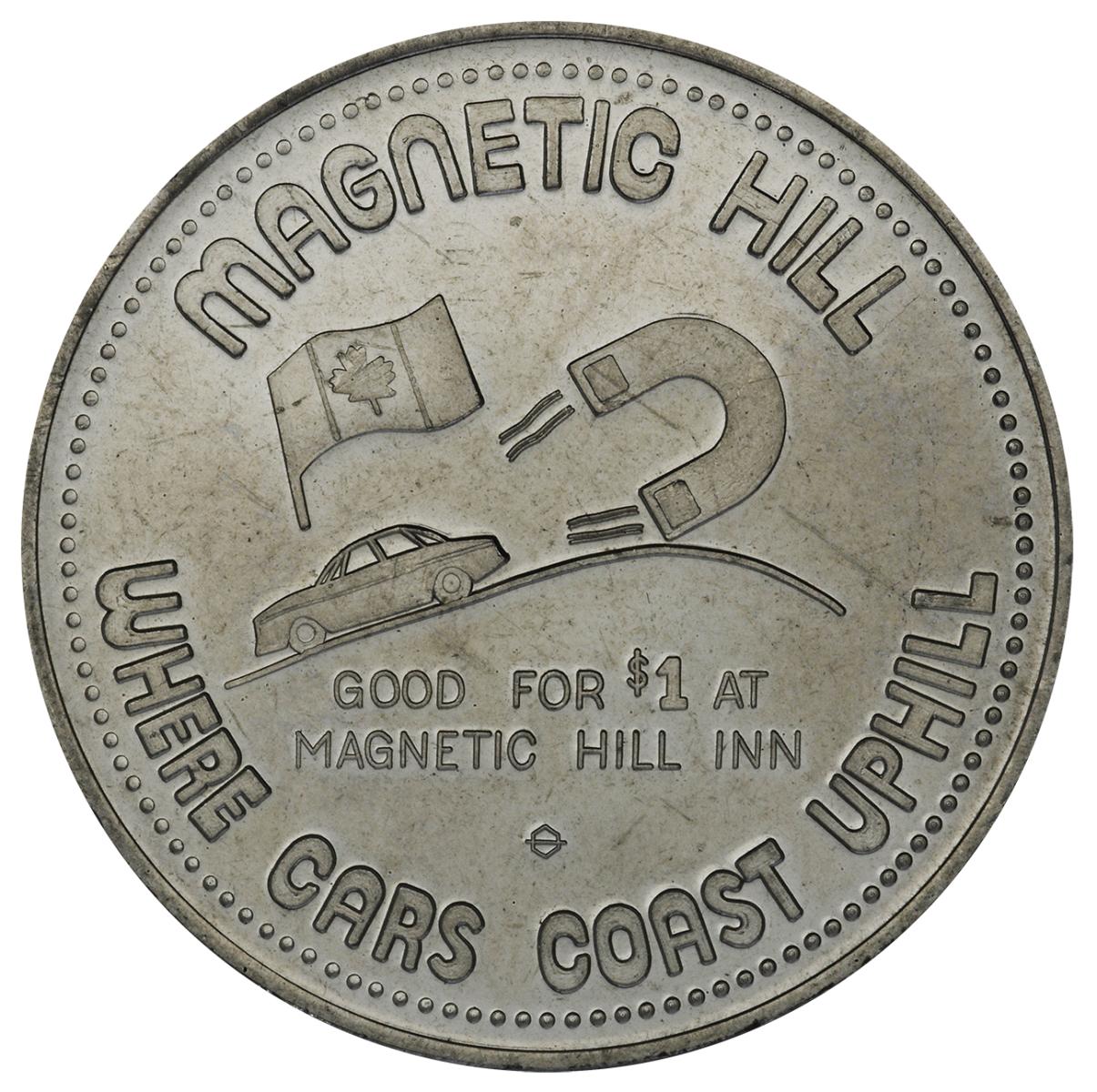 Souvenir token Token, round, grey, a car pointed down a slope with a giant magnet behind it.